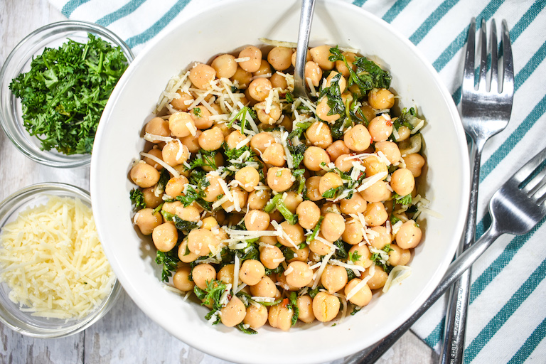 Chickpea salad in a white bowl, accompanied by small bowls of herbs and cheese