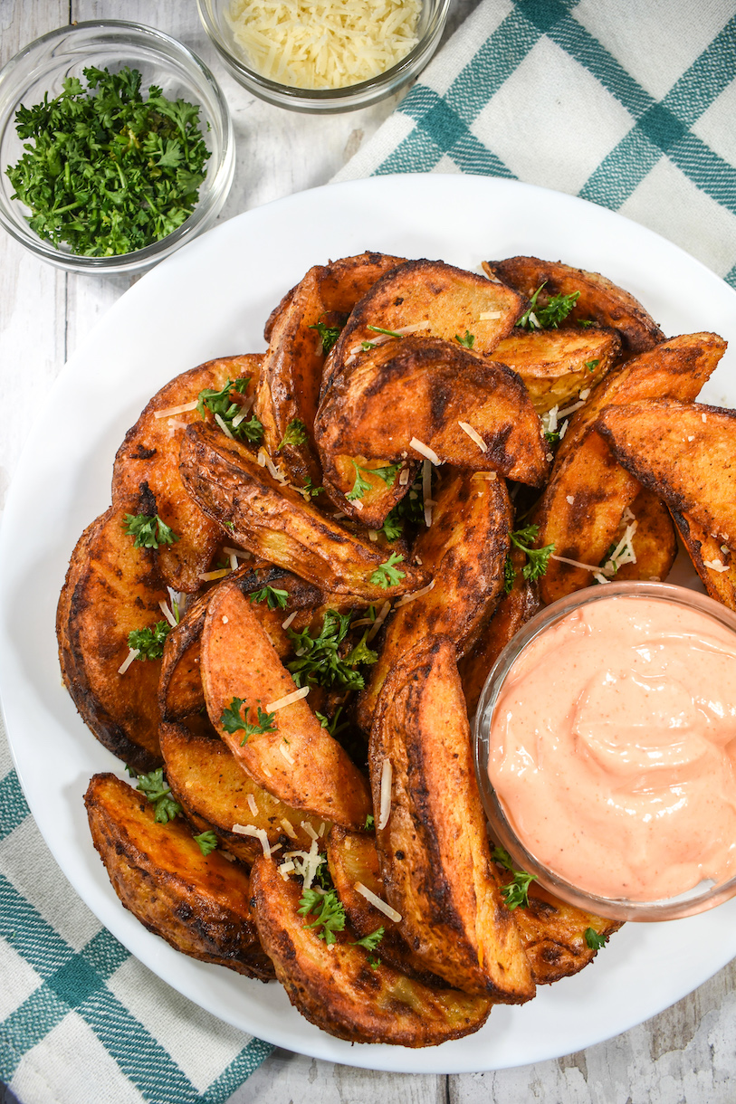 Roasted potato wedges on a plate with a dish of sriracha mayo