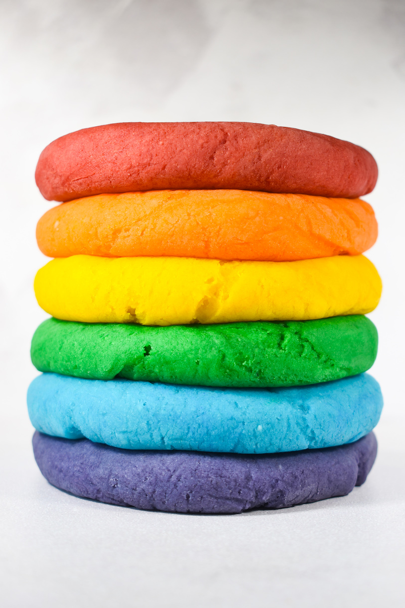 A rainbow stack of homemade playdough against a white backdrop