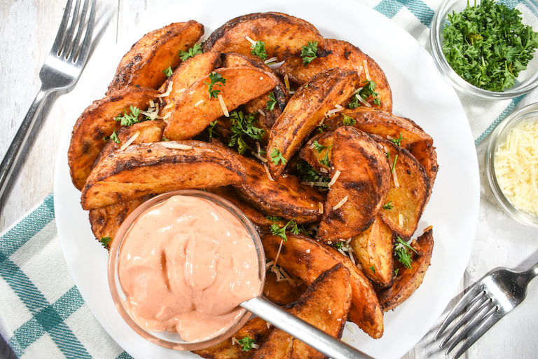 Spicy potato wedges on a plate with a bowl of sriracha mayonnaise