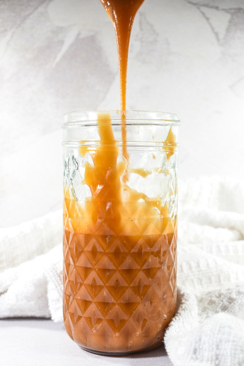 A spoon drizzling caramel sauce into a jar