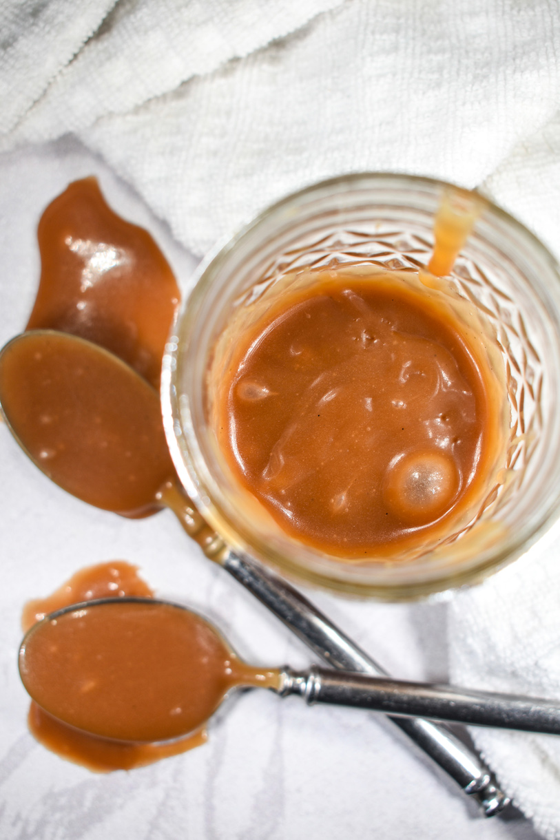 A jar of caramel sauce and two caramel-covered spoons