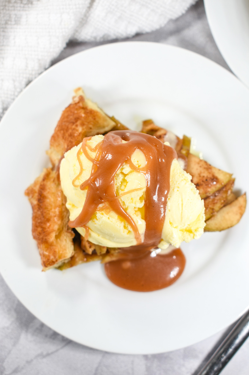 An apple galette with ice cream and caramel sauce on a white plate
