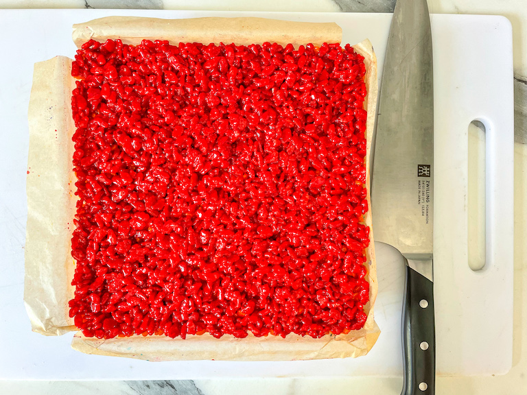 Red krispie treat slab on cutting board with knife