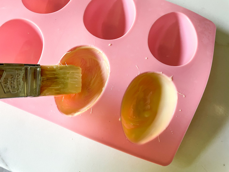 Brushing melted chocolate into a pink egg mould