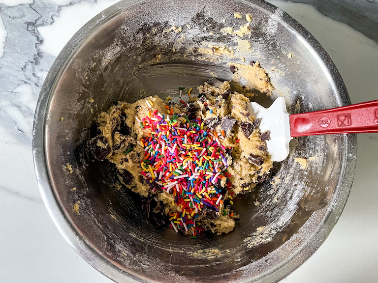 Adding rainbow sprinkles to a bowl of chocolate chip cookie dough