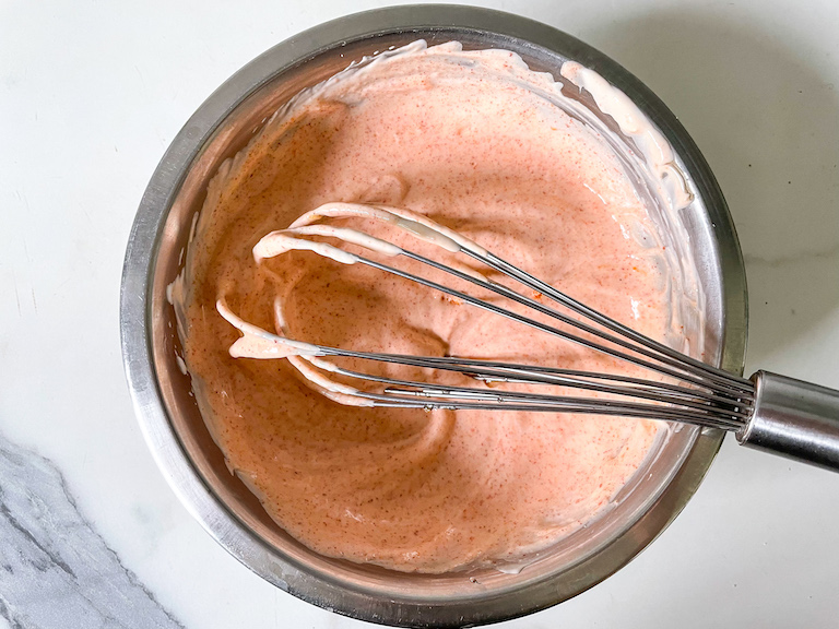 A bowl of sriracha dip with a whisk