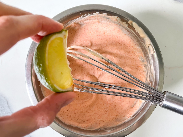 Hand squeezing lime into a bowl of Greek yogurt dip