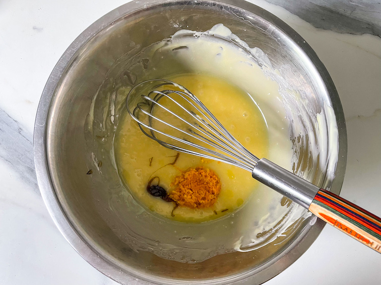White chocolate, orange zest, and vanilla bean paste in a bowl with a whisk