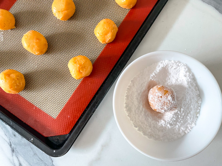 Rolling creamsicle truffles in a bowl of powdered sugar