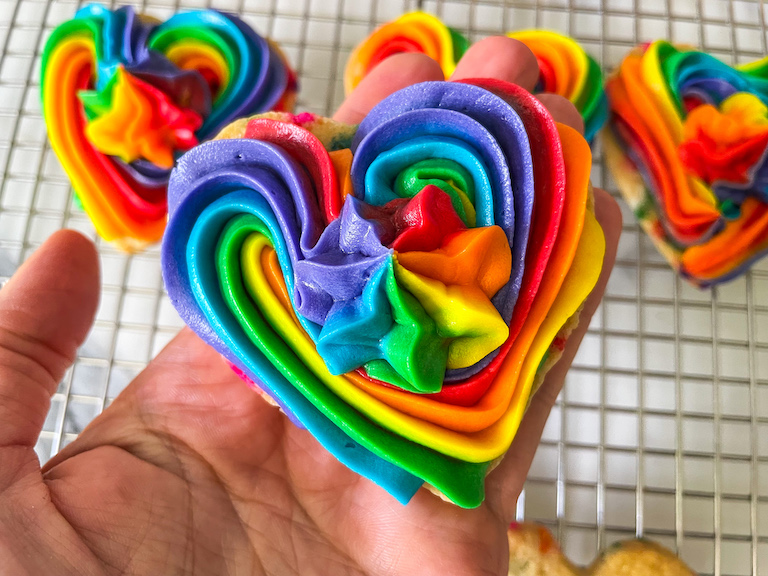 hand holding a buttercream rainbow heart cookie