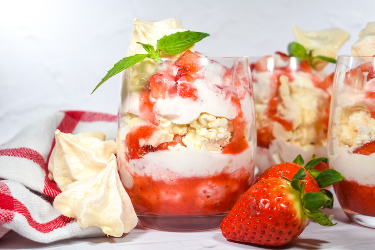 Eton Mess in a glass, along with meringues, strawberries, and a striped towel