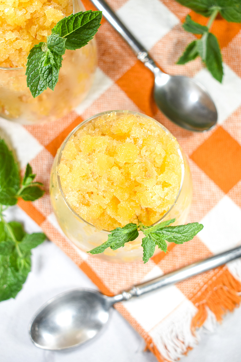 A glass of peach granita on a plaid towel with a spoon