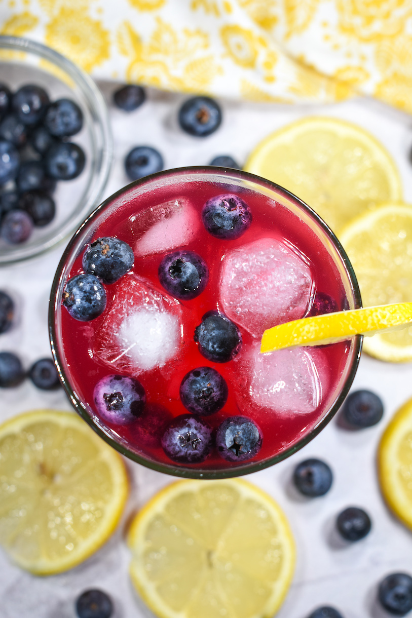 A glass of blueberry lemonade surrounded by berries and lemon slices