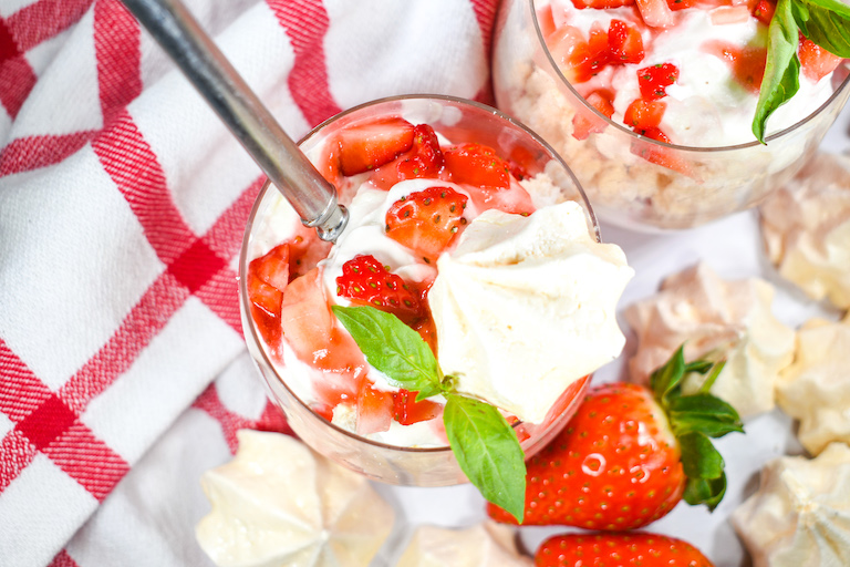 Looking down at an Eton Mess in a glass, along with meringues and fresh strawberries