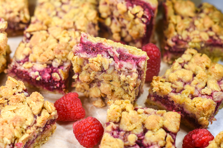 Raspberry bars and fresh raspberries arranged on parchment