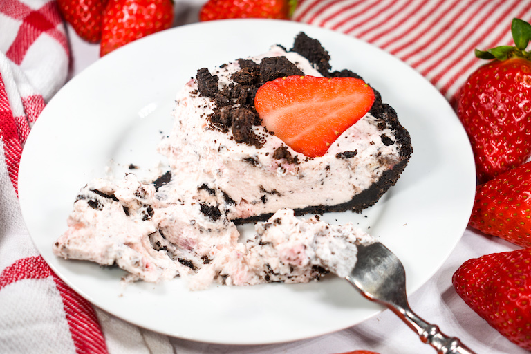 Slice of no bake Oreo pie on a white plate garnished with a strawberry