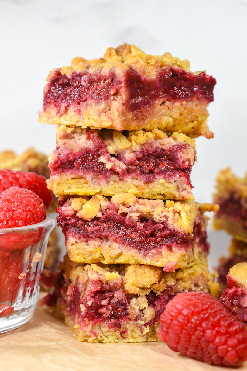 A stack of four raspberry bars next to a dish of fresh berries