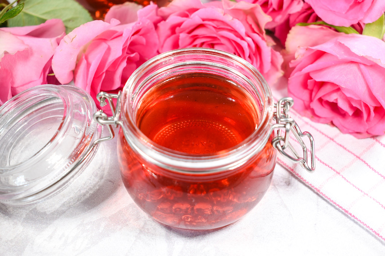 A jar of rose syrup surrounded by pink roses