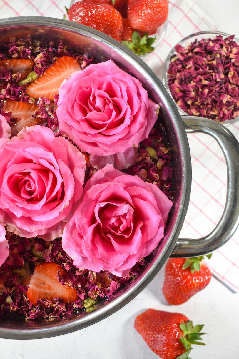 Vertical shot of a rose simmer pot potpourri surrounded by strawberries and rose petals