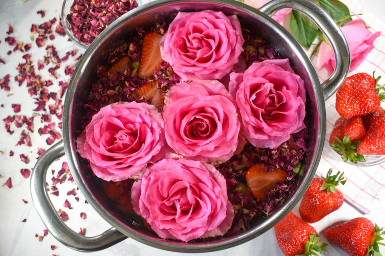 A rose simmer pot surrounded by strawberries and rose petals