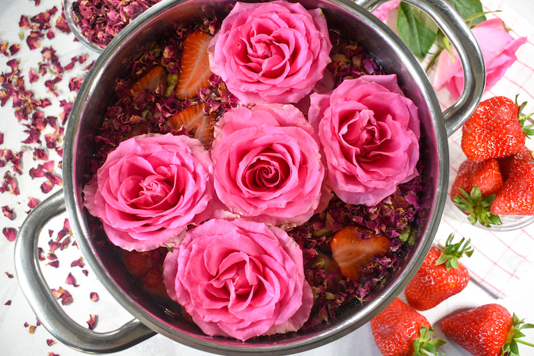 A simmer pot with pink roses, surrounded by strawberries and dried rose petals