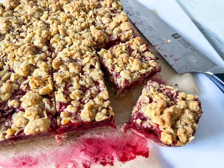 A slab of raspberry crumble bars on a cutting board with a knife