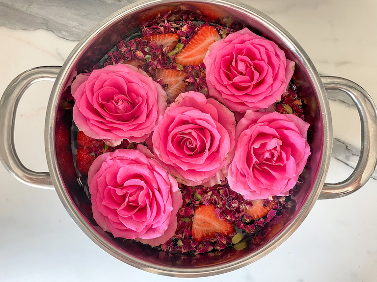 Saucepan filled with roses, strawberries, and cardamom pods