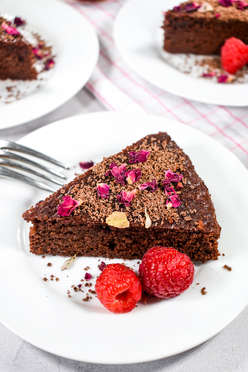 A slice of chocolate cake on a plate with two raspberries and a fork