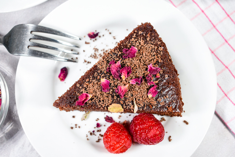 Horizontal shot of a single slice of chocolate almond cake garnished with dried rose petals and raspberries