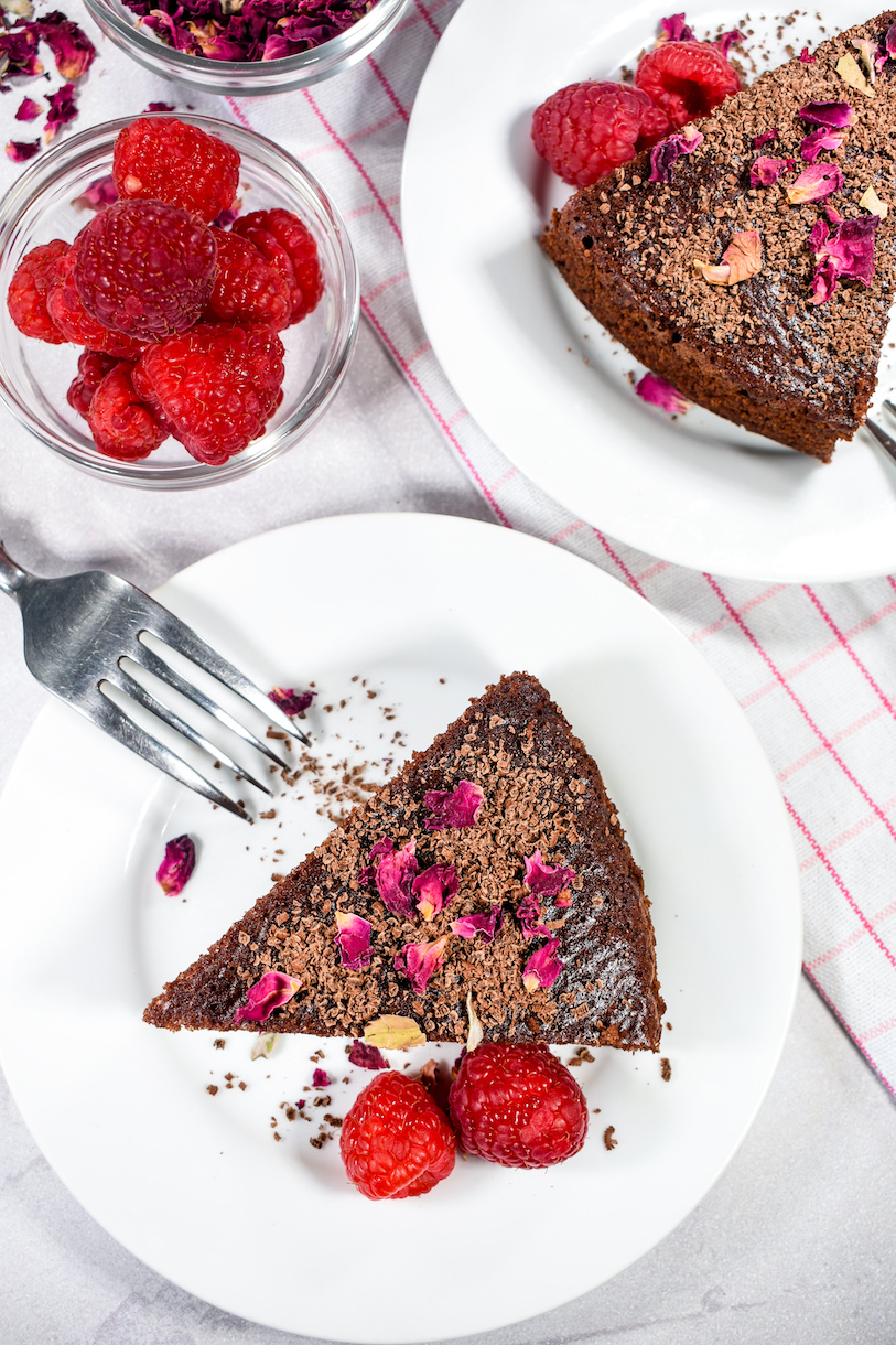 A slice of chocolate cake on a plate with two raspberries