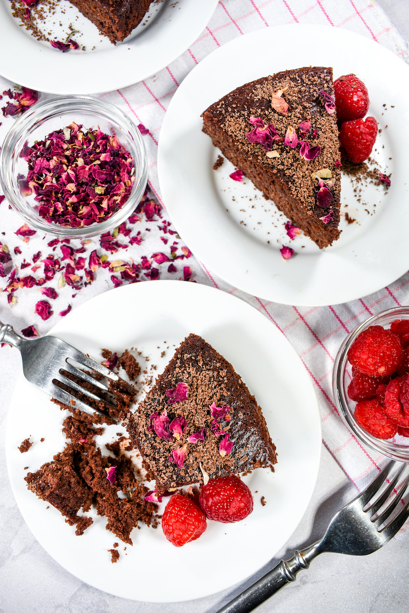 Slices of chocolate cake on plates with rose and raspberry garnishes