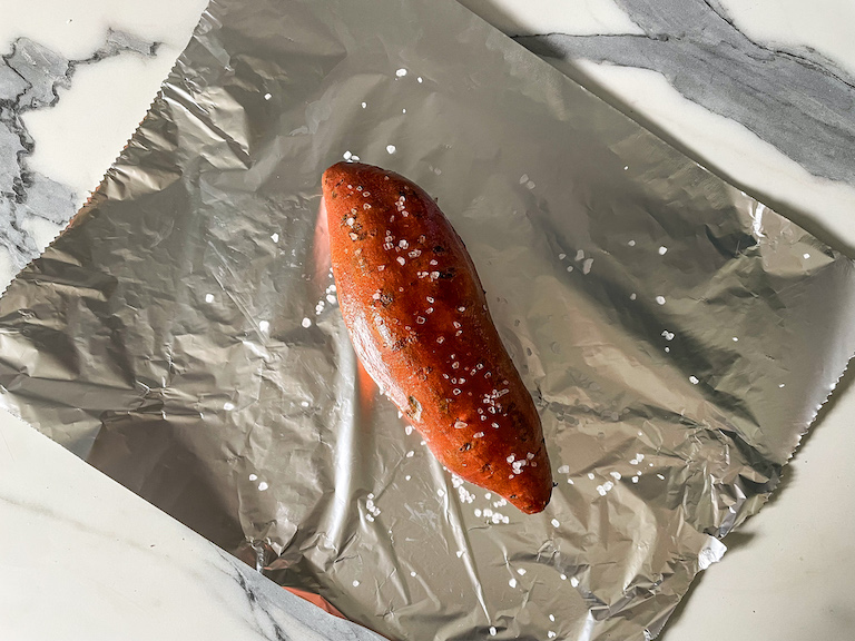 A sheet of foil with a sweet potato sprinkled in sea salt