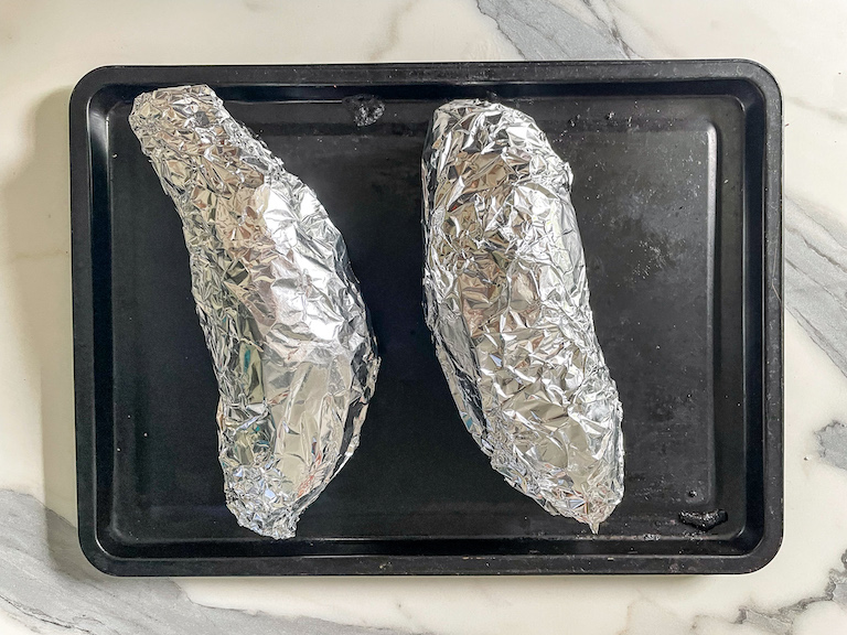 Foil-wrapped sweet potatoes on a small tray