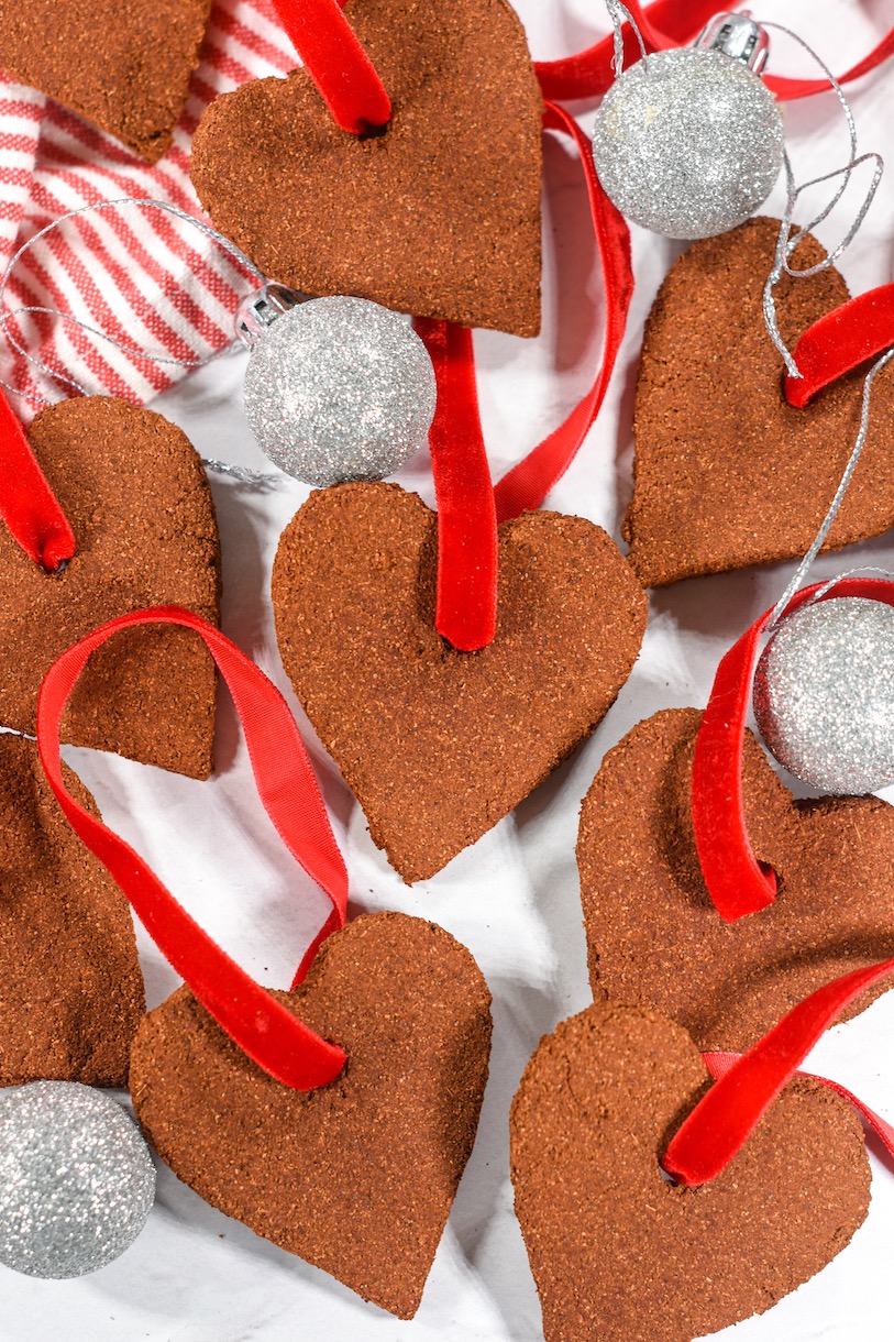 Applesauce ornaments with red ribbons, arranged on a white surface with silver Christmas balls