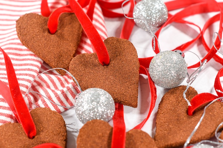 Applesauce ornaments with red ribbons, arranged on a white surface with silver Christmas balls