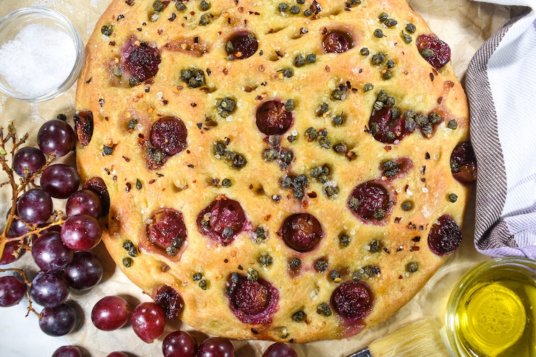 Loaf of focaccia, bunch of grapes, and dishes of sea salt and olive oil