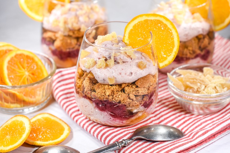 Cranberry and orange parfait in a clear wine glass, garnished with a slice of fresh orange