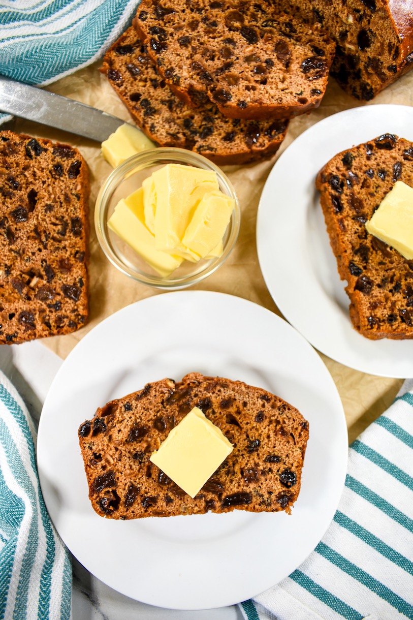 Slices of Welsh bara brith bread on white plates along with a bowl of butter