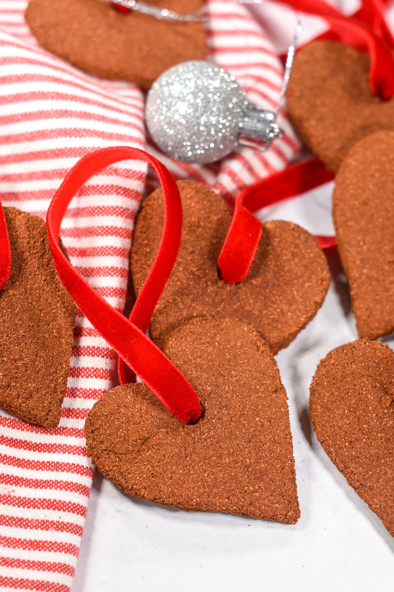 Applesauce ornaments with red ribbons, arranged on a white surface with silver Christmas balls