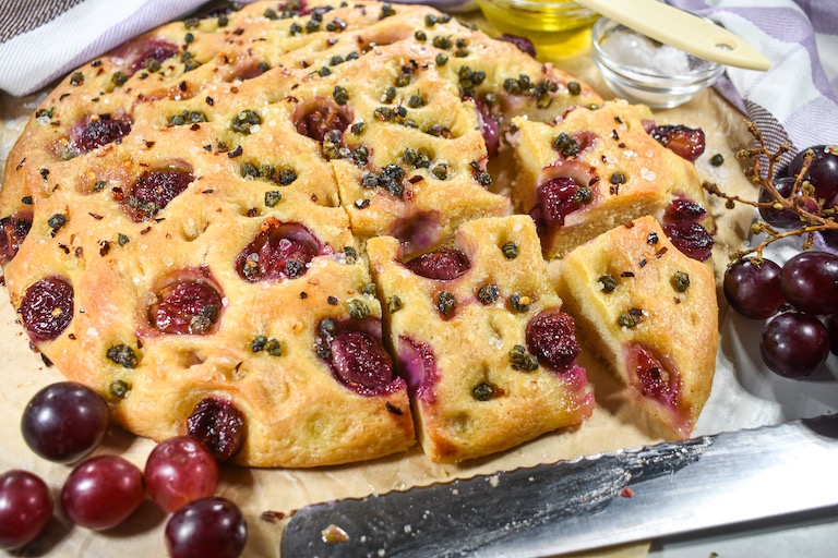 A loaf of grape focaccia with a knife and red grapes