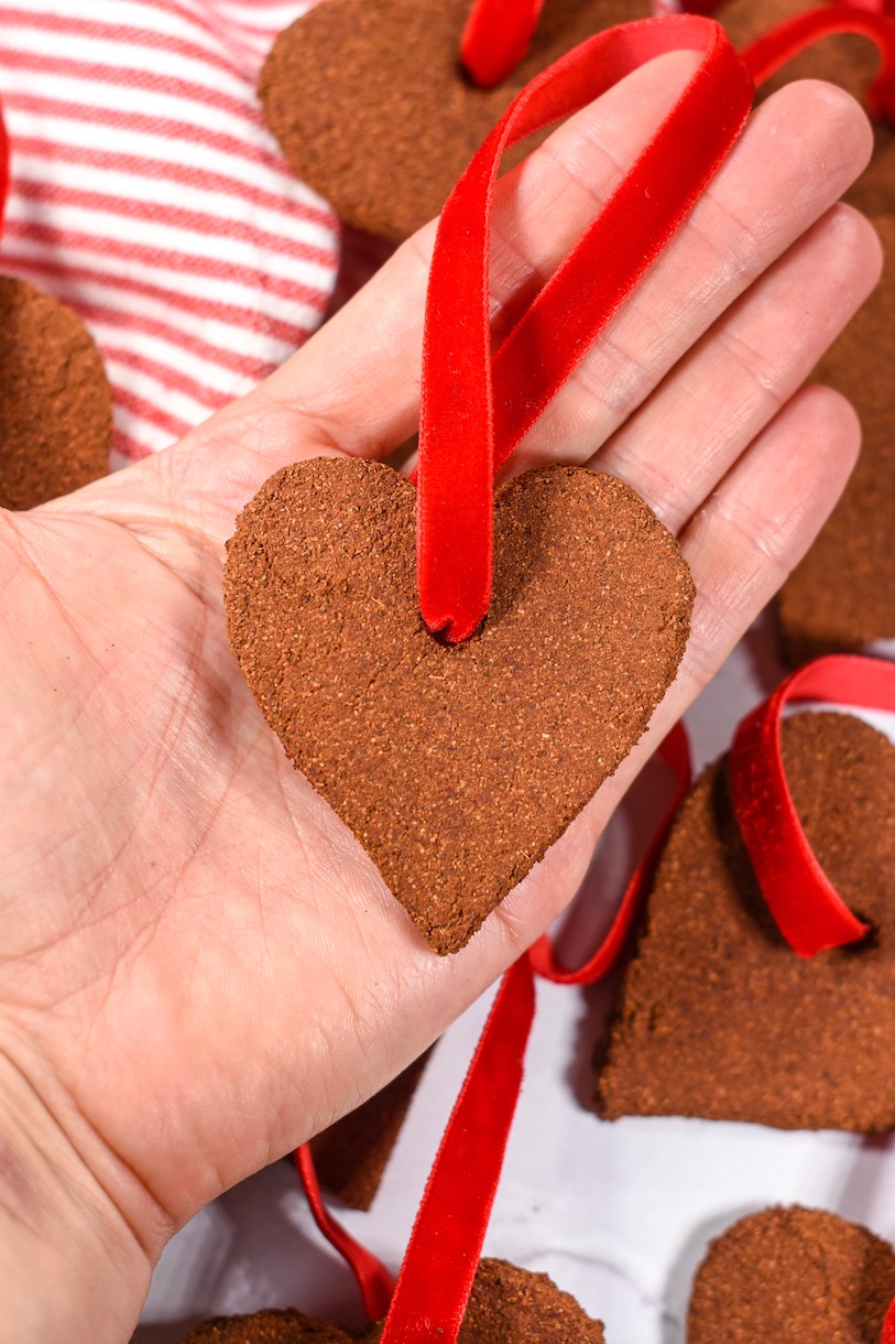 Hand holding a heart shaped cinnamon ornament with a red velvet ribbon