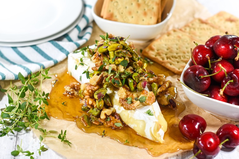 Baked brie piled with honey, nuts, and thyme, surrounded by cherries and crackers