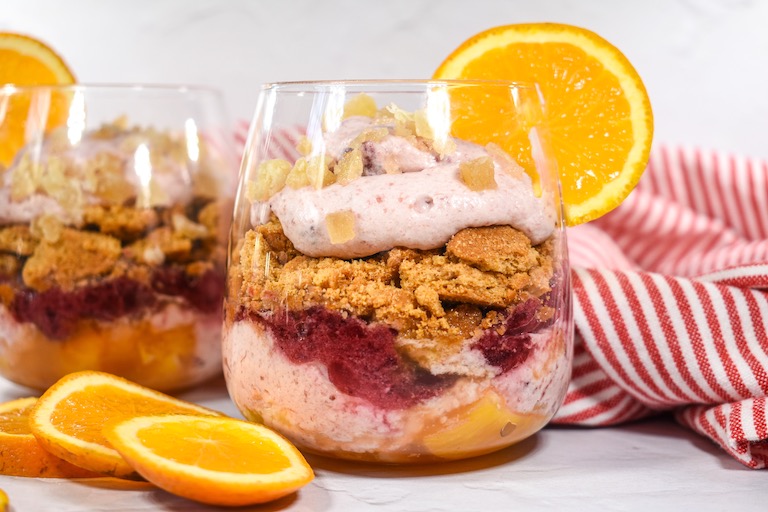 Cranberry and orange parfait in a clear wine glass, garnished with a slice of fresh orange