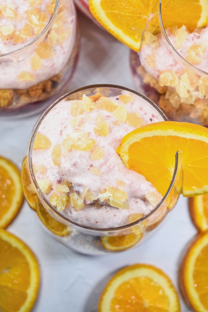 Looking down at a cranberry and orange parfait in a clear wine glass, garnished with a slice of fresh orange