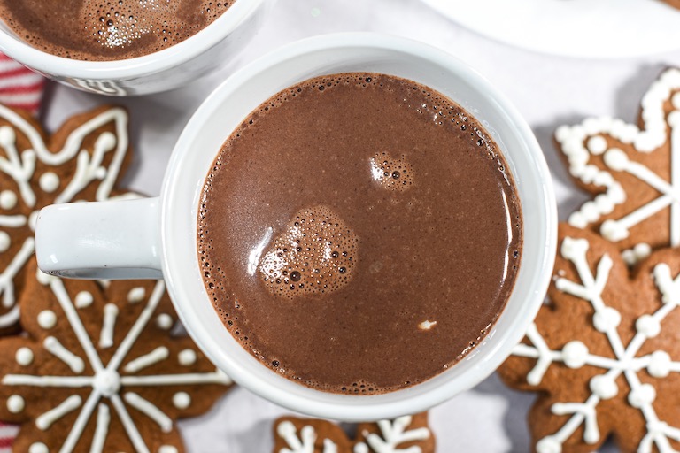 A mug of gingerbread hot chocolate surrounded by snowflake shaped gingerbread cookies