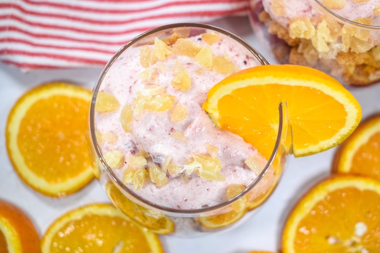 Cranberry and orange parfait in a clear wine glass, garnished with a slice of fresh orange