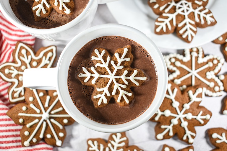 A mug of gingerbread hot chocolate surrounded by snowflake shaped gingerbread cookies