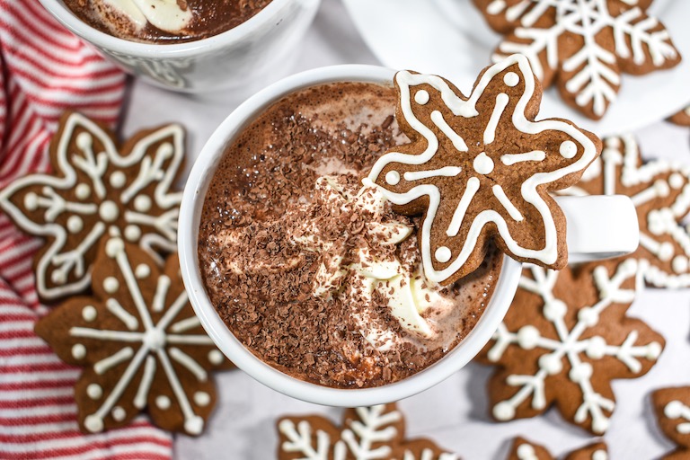 A mug of gingerbread hot chocolate surrounded by snowflake shaped gingerbread cookies