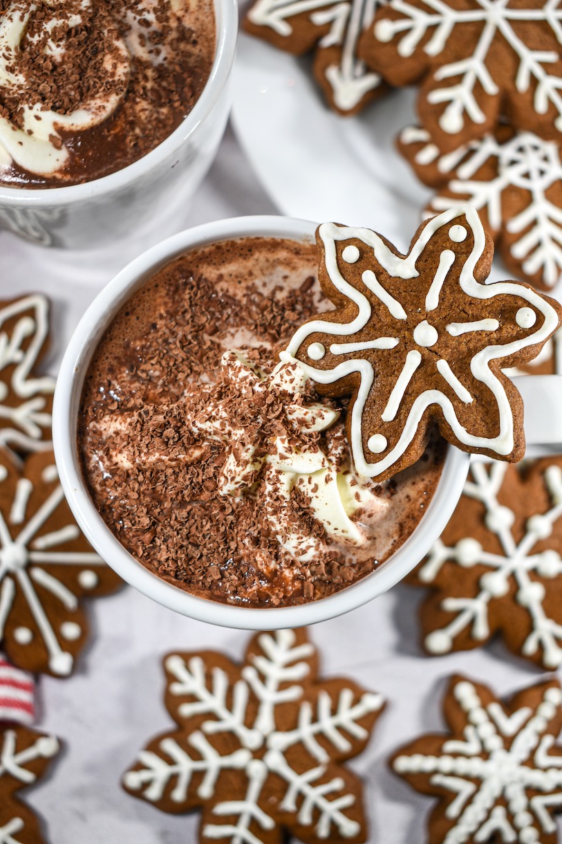 A mug of gingerbread hot chocolate surrounded by snowflake shaped gingerbread cookies